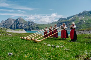 Fünf Damen die Alphorn spielen am malerischen Ufer des Lünersee | © Golm Silvretta Lünersee Tourismus GmbH Bregenz, Philipp Schilcher