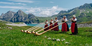 Fünf Damen die Alphorn spielen am malerischen Ufer des Lünersee | © Golm Silvretta Lünersee Tourismus GmbH Bregenz, Philipp Schilcher
